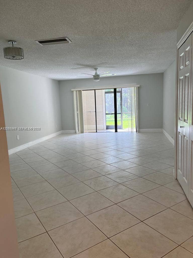 21362 Juego Circle, #33E, Boca Raton, Boca Raton, FL 33433 Spacious room featuring tile flooring, a ceiling fan, a drum-style pendant light, and a sliding glass door to access a screened lanai with conservation views