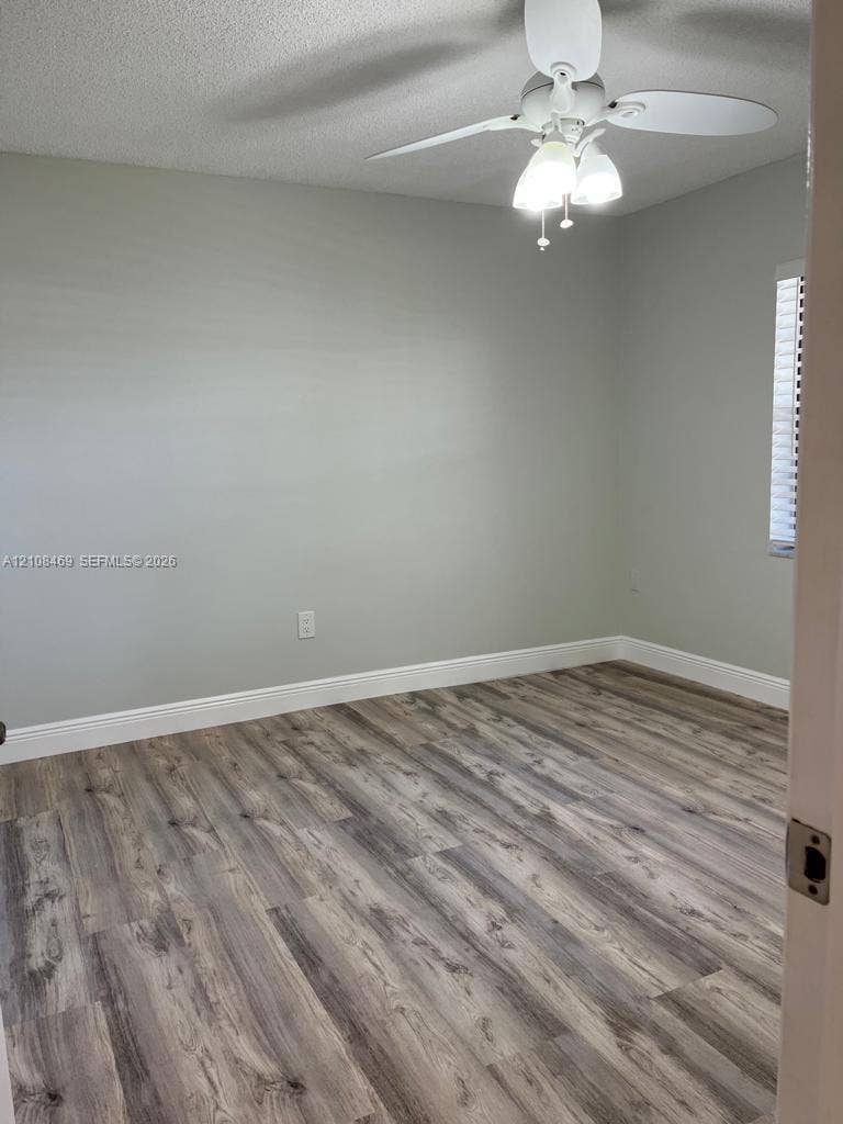 21362 Juego Circle, #33E, Boca Raton, Boca Raton, FL 33433 Wood-finish flooring, neutral wall tones, white ceiling fan with integrated three-light fixture, and window blinds