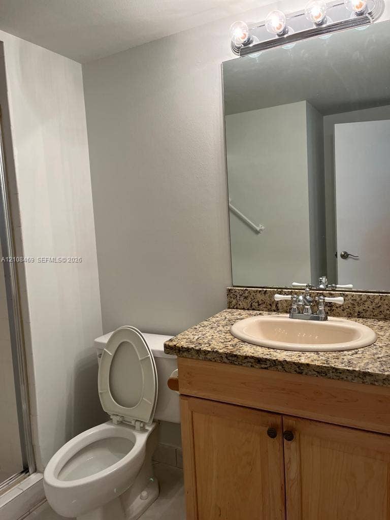 21362 Juego Circle, #33E, Boca Raton, Boca Raton, FL 33433 Bathroom with shower, vanity featuring a natural stone countertop, undermount sink, light wood cabinetry, and a multi-bulb vanity light fixture above a wall-mounted mirror