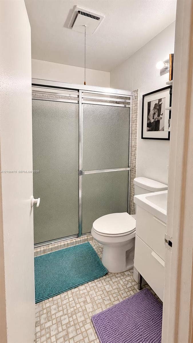 Shower featuring a sliding glass enclosure with metal frame, mosaic-tiled accent wall, vanity with integrated basin, and patterned tile flooring