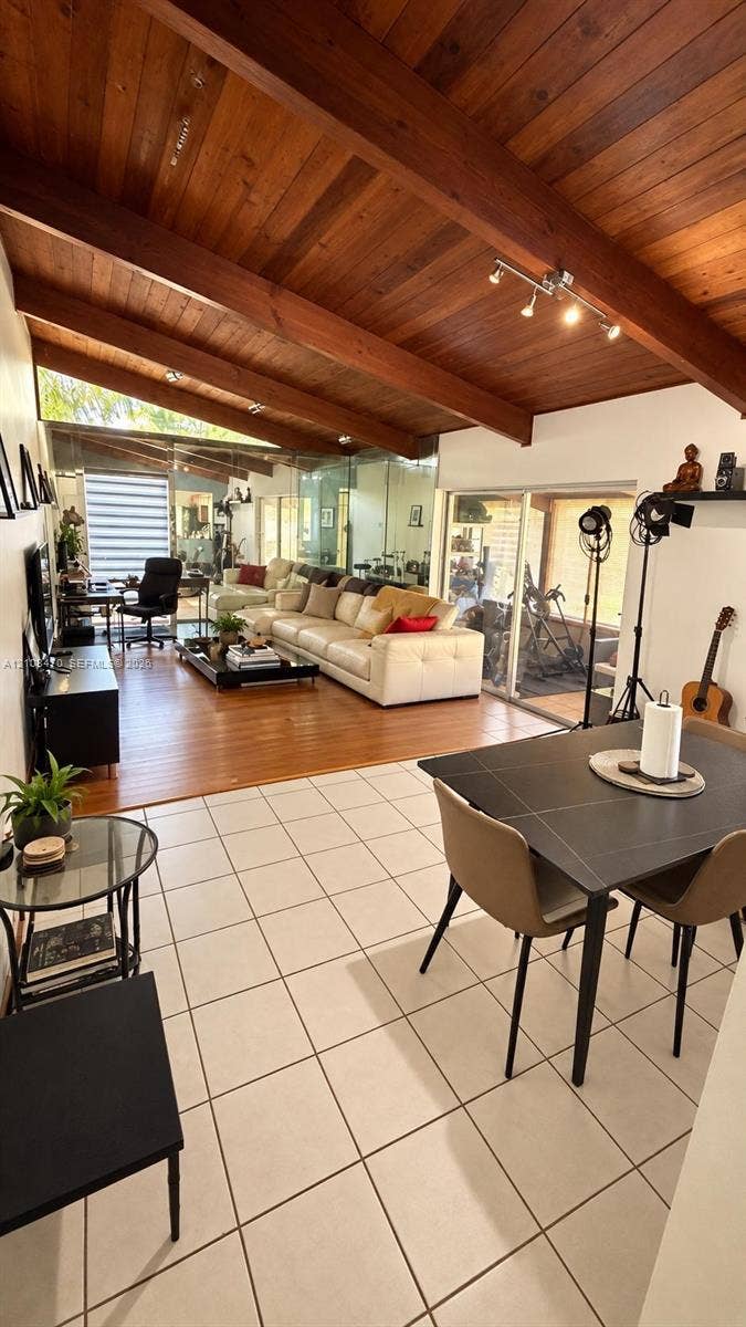 Vaulted timber-plank ceiling featuring exposed structural beams, wood-finish flooring, and large-format ceramic floor tiles