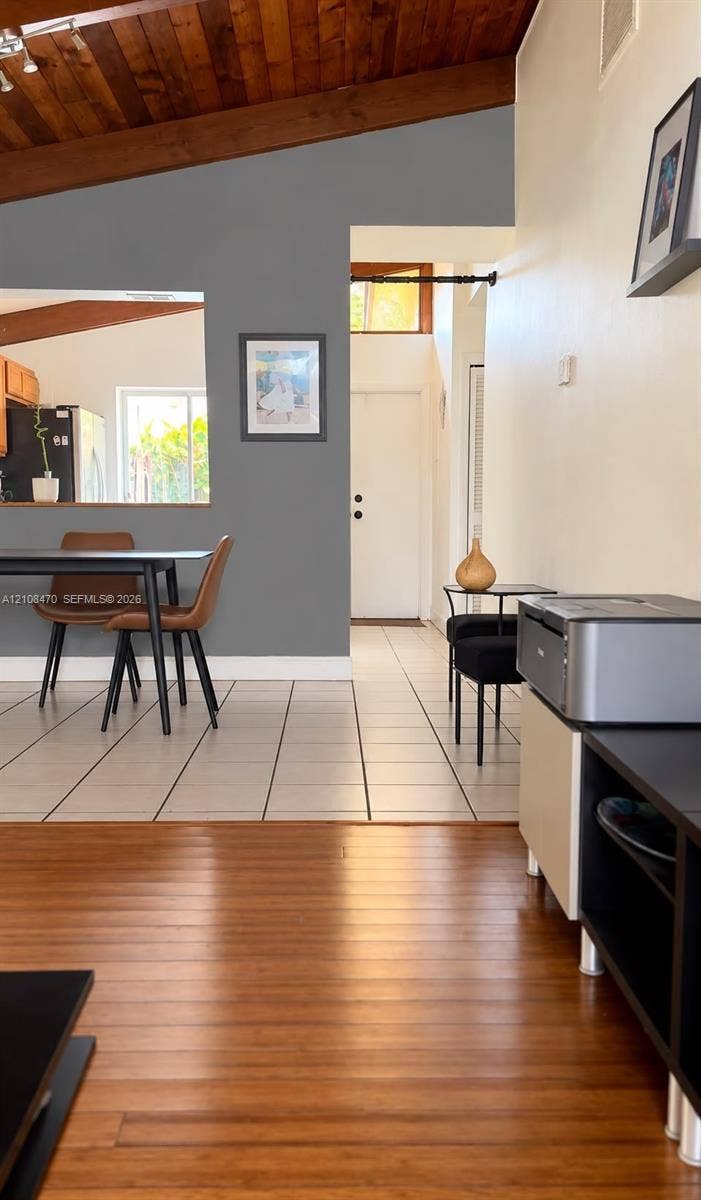 Vaulted ceiling with exposed wooden beams, natural wood-finish flooring, and ceramic tile flooring
