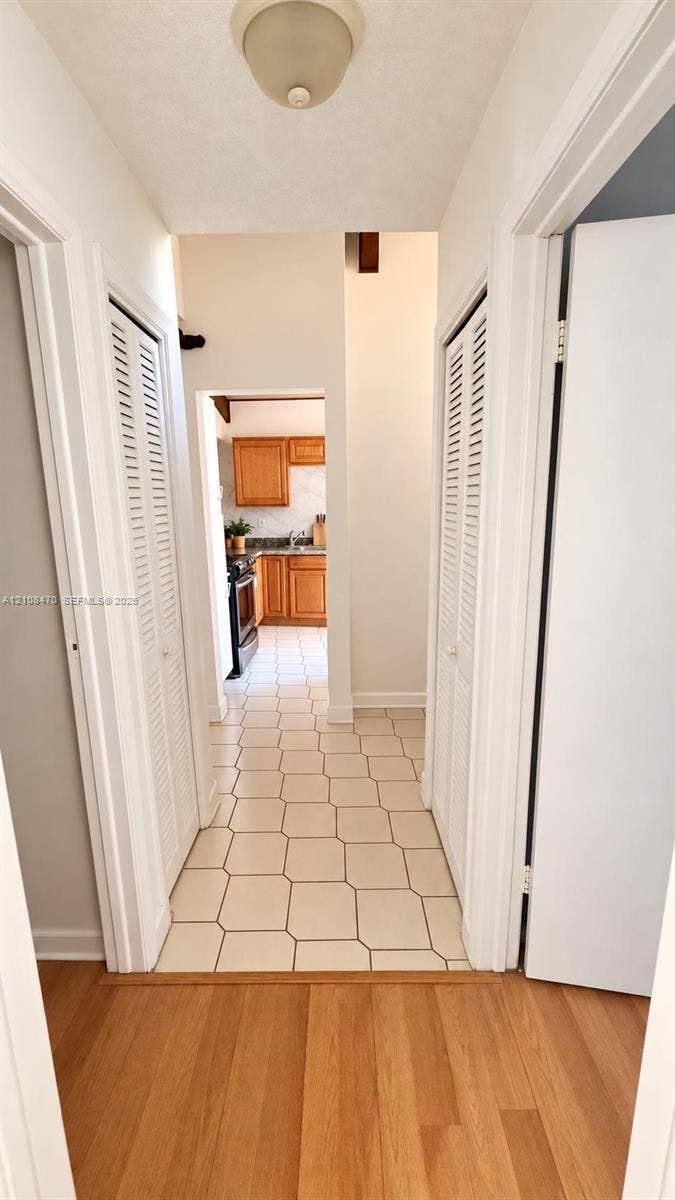 Hallway featuring wood-finish flooring, dual louvered-style closet doors, geometric tile flooring, and a flush-mount ceiling fixture