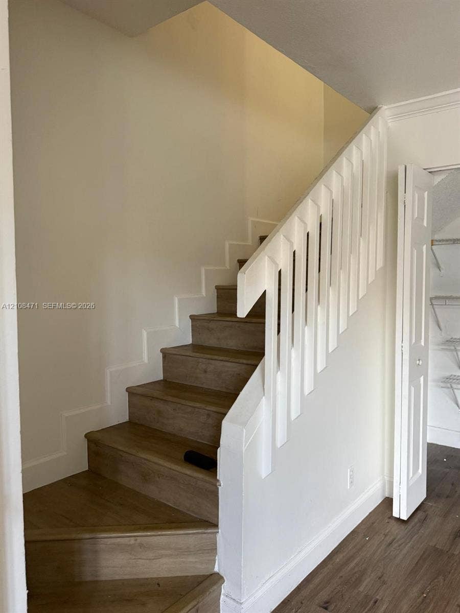 Staircase featuring wood-finish treads, a white handrail with vertical balusters, and a built-in closet with wire shelving