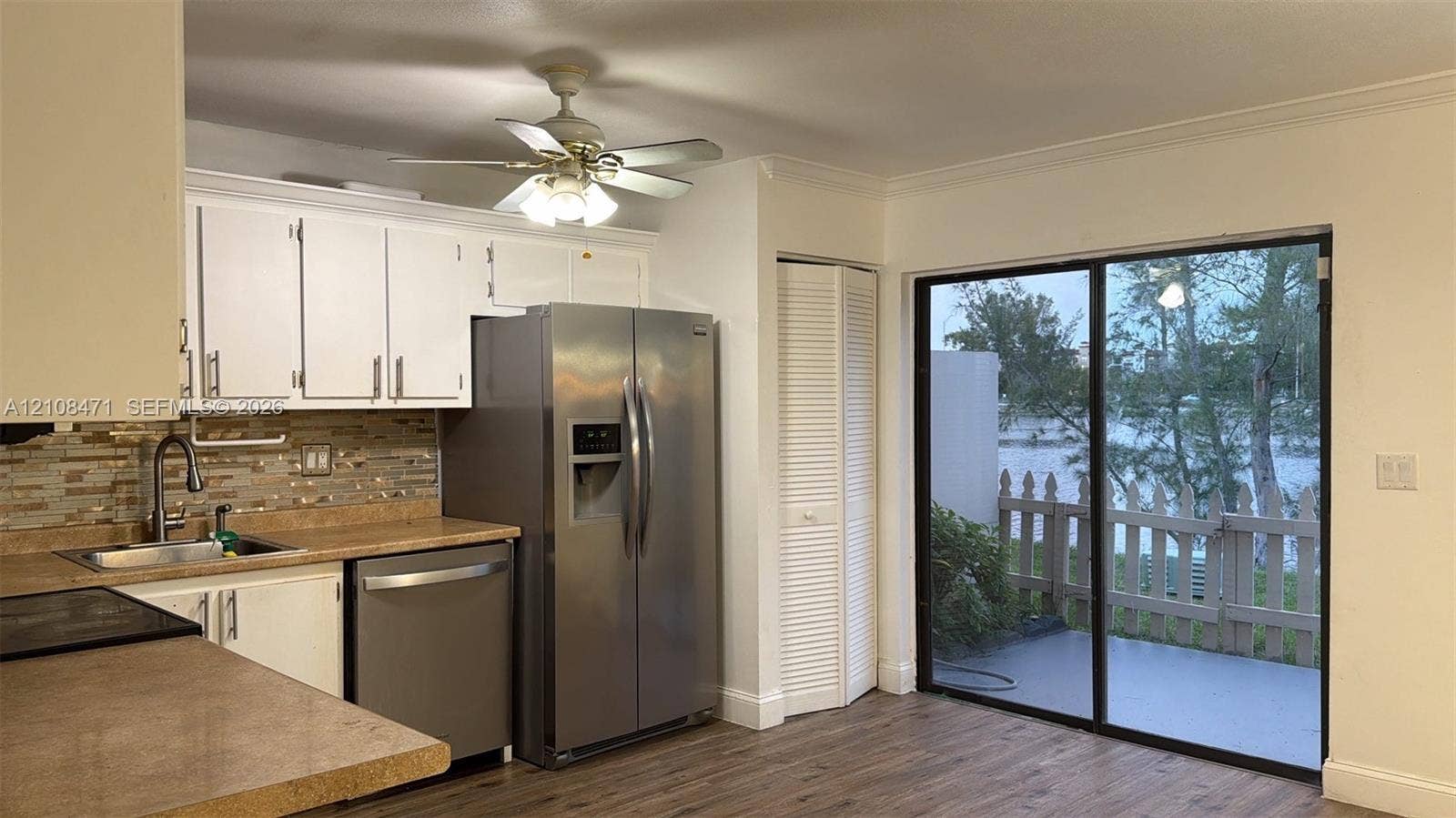 Kitchen featuring white cabinetry, stainless steel appliances, multi-toned stone-tile backsplash, wood-finish flooring, and sliding glass doors with access to an exterior patio