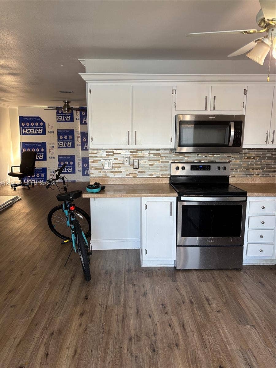 Kitchen featuring white cabinetry, wood-finish flooring, stainless steel appliances, and a glass-tile backsplash