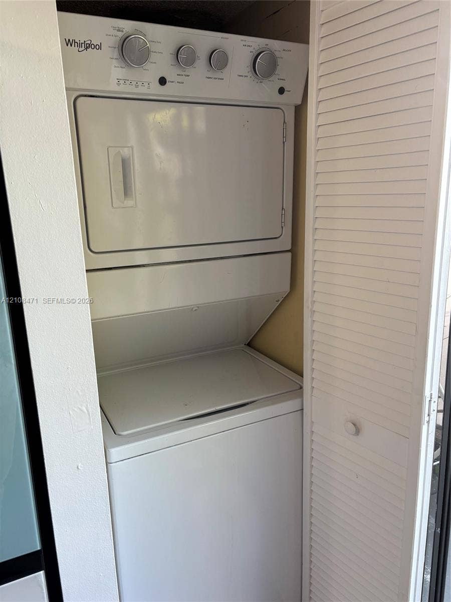 Stacked washer and dryer unit housed within a closet featuring white louvered doors