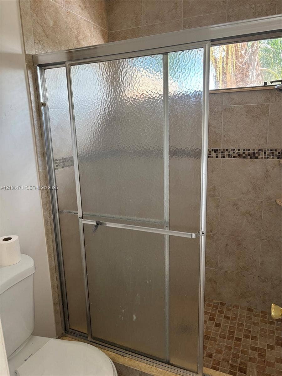 Shower enclosure featuring textured glass sliding doors, metal framing, square ceramic wall tile, a decorative glass mosaic tile inlay, and square-patterned floor tile