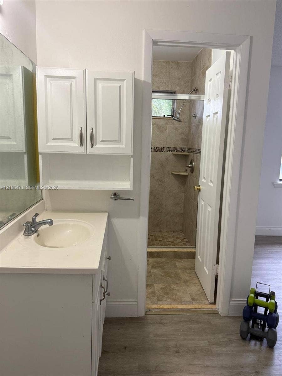Bathroom featuring a white vanity cabinet with an integrated sink, wall-mounted upper storage cabinetry, full-width mirror, and a tiled shower enclosure with built-in corner shelving