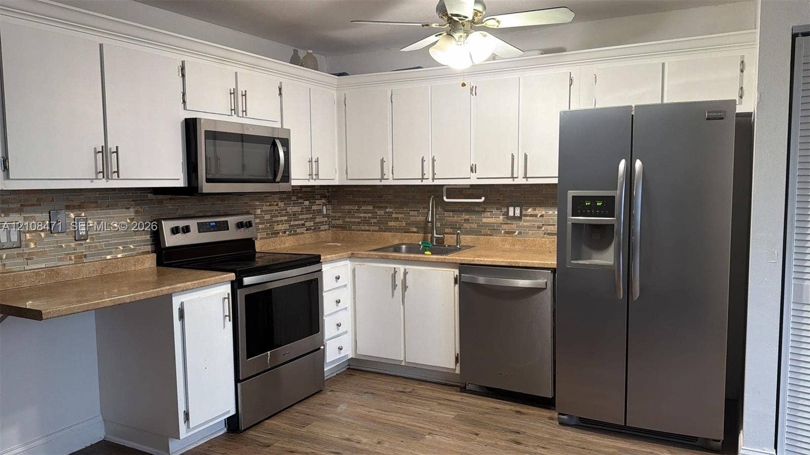 Kitchen featuring white cabinetry, stainless steel appliances, multi-toned tile backsplash, solid-surface countertops, and wood-finish flooring