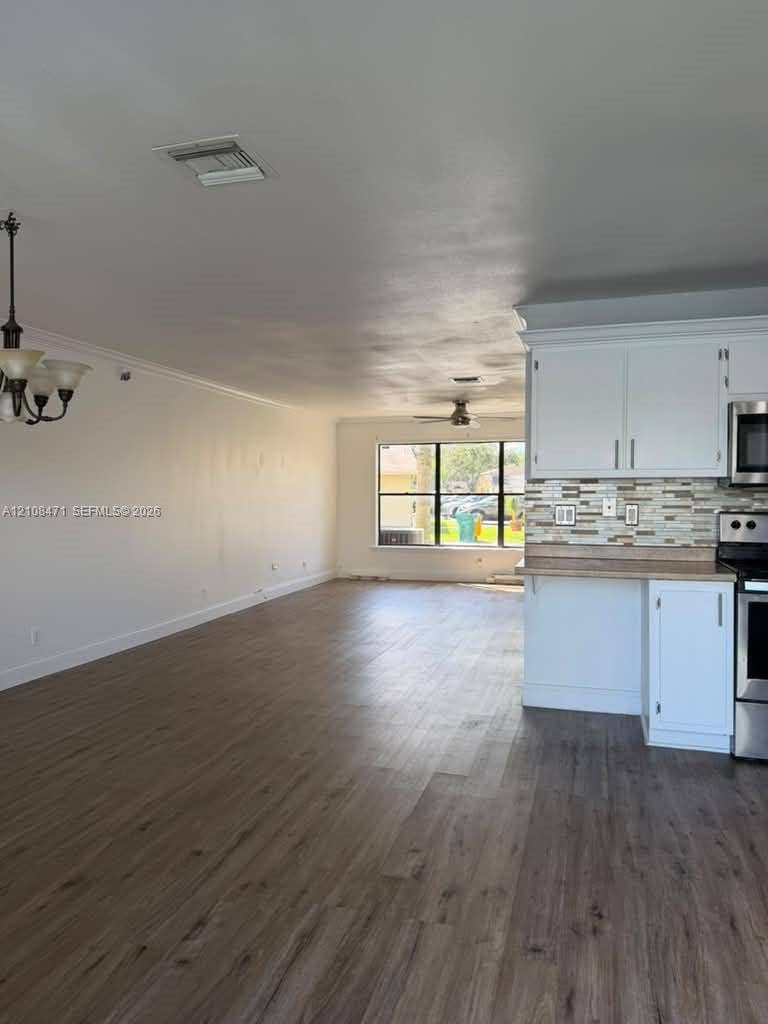 Wood-finish flooring, white cabinetry, decorative tile backsplash, stainless steel appliances, and multi-light chandelier