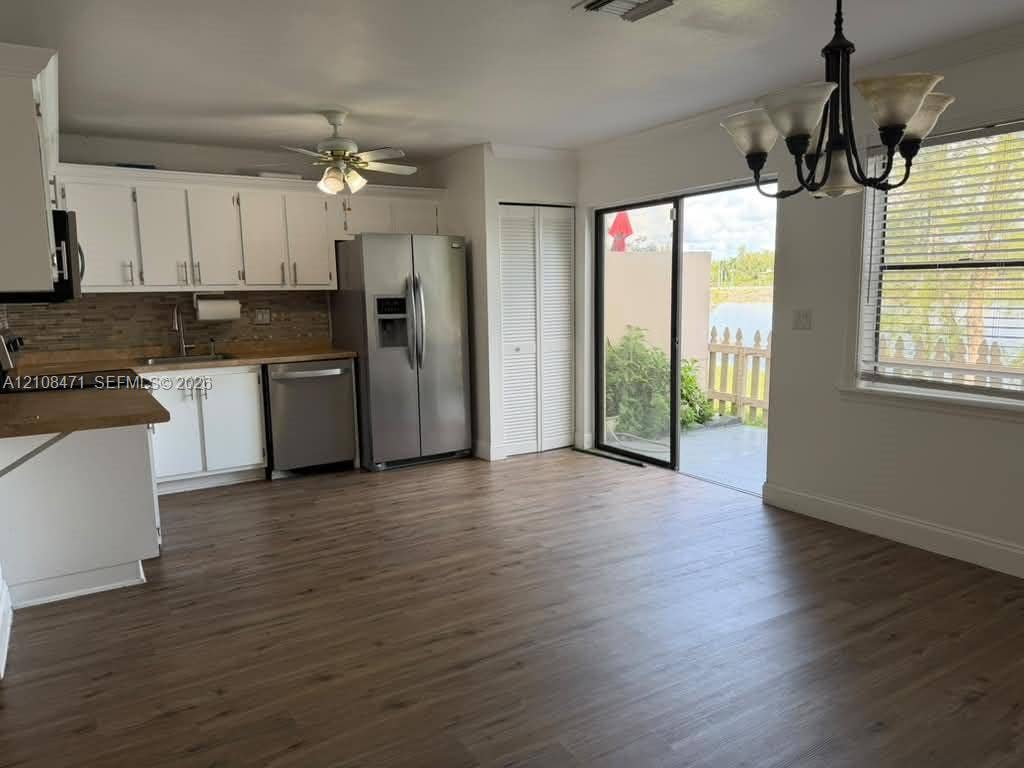 Kitchen featuring white shaker-style cabinetry, wood-finish flooring, stainless steel appliances, tiled backsplash, and sliding glass doors