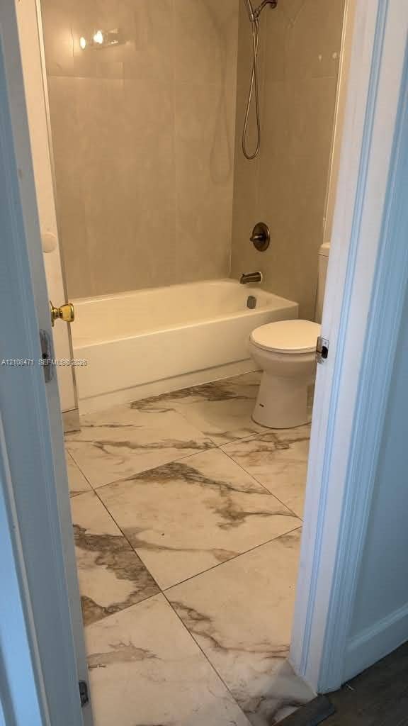 Bathroom featuring large-format tile flooring with a neutral veined pattern, a porcelain bathtub, and wall-mounted shower hardware in a metallic finish