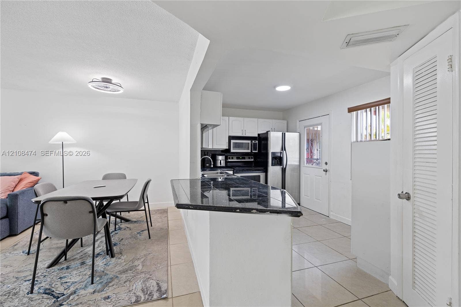1501 NE 191st Street, #C216, Miami, FL 33179 Kitchen featuring dark stone-surfaced breakfast bar, white cabinetry, integrated stainless steel appliances, and neutral tile flooring throughout