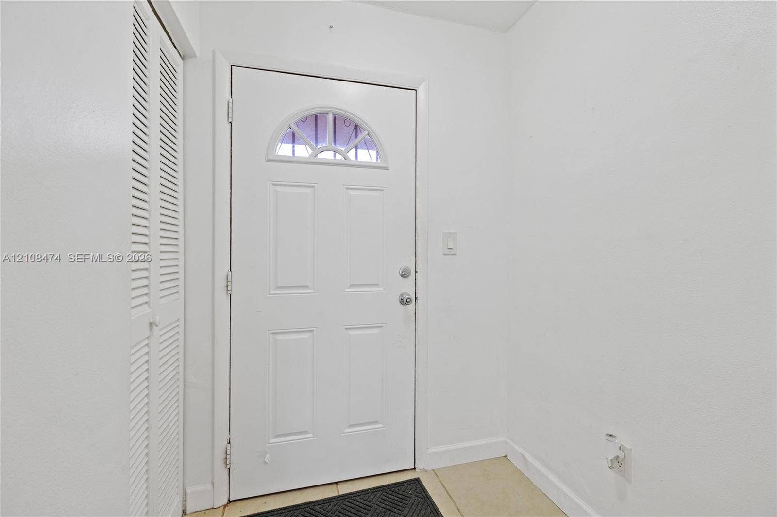 1501 NE 191st Street, #C216, Miami, FL 33179 Entryway featuring a four-panel door with a semi-circular transom window and a floor-to-ceiling closet with louvered double doors