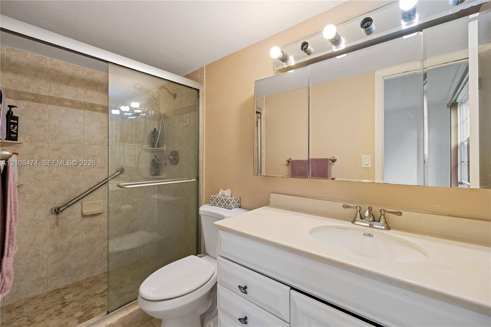 1501 NE 191st Street, #C216, Miami, FL 33179 Bathroom featuring a vanity with white cabinetry, a light-toned countertop, an integrated sink, a glass-enclosed shower with tiled surround, and a tri-fold medicine cabinet with attached vanity lighting