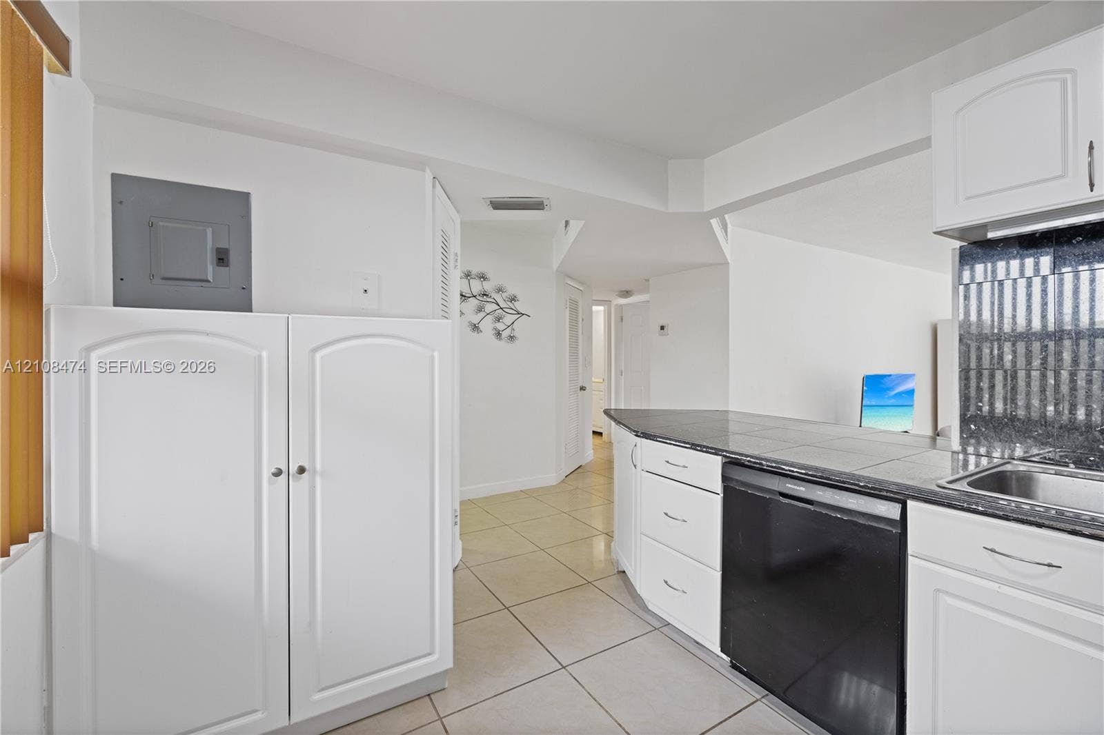 1501 NE 191st Street, #C216, Miami, FL 33179 Kitchen featuring white shaker-style cabinetry, dark stone-finish countertops, tiled flooring, and a stainless steel built-in dishwasher