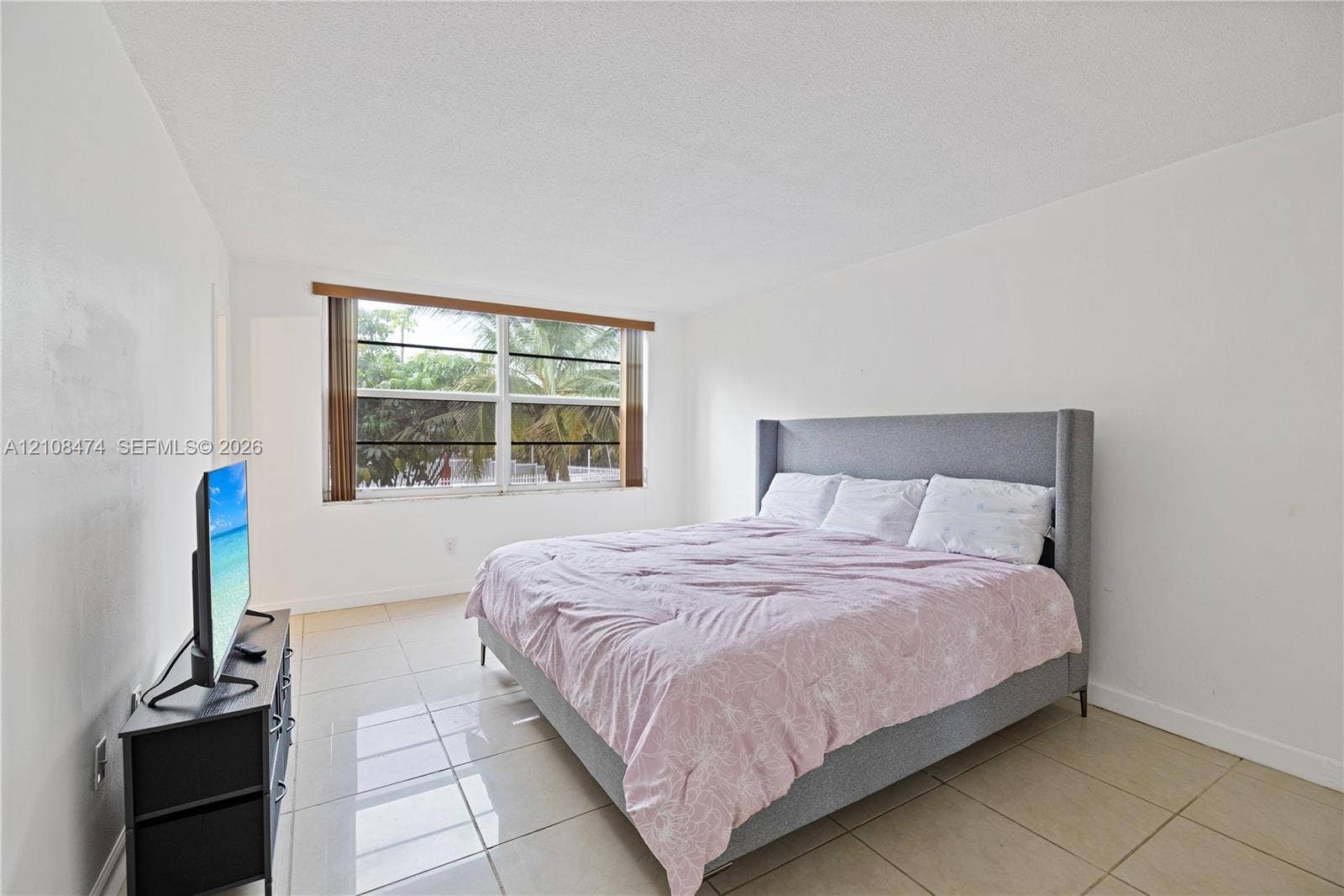 1501 NE 191st Street, #C216, Miami, FL 33179 Neutral-toned interior space featuring light-colored large-format tile flooring, expansive window with horizontal blind hardware, and crisp white wall finishes