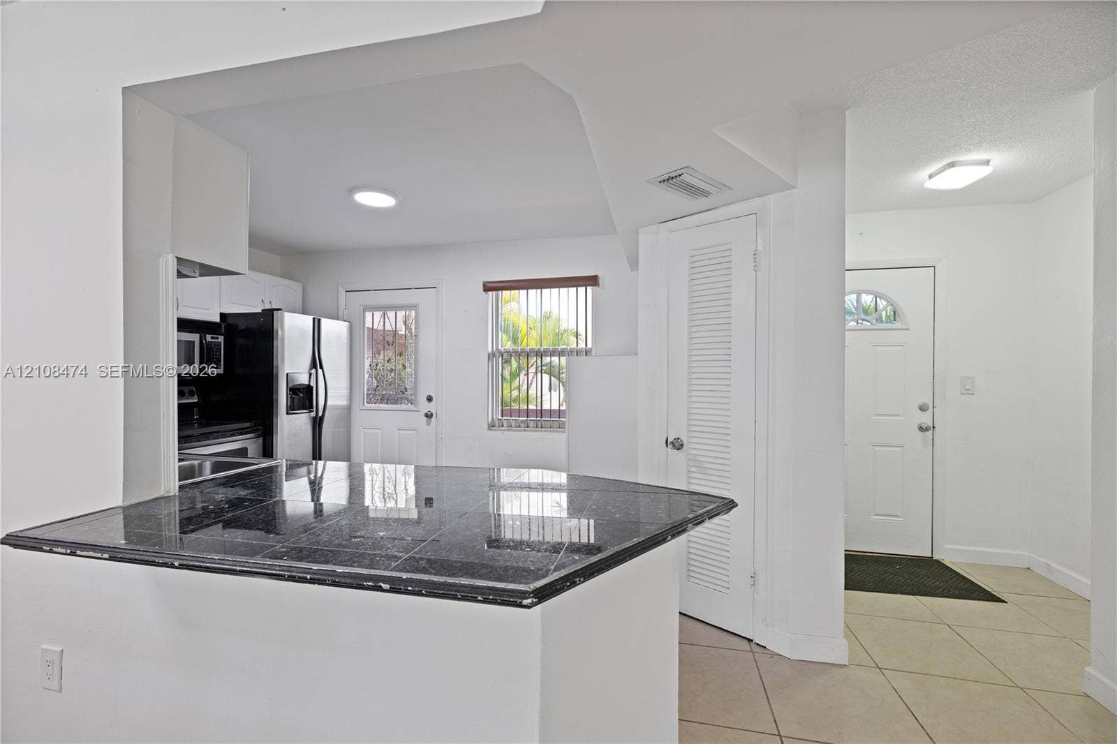 1501 NE 191st Street, #C216, Miami, FL 33179 Kitchen featuring stone-surfaced breakfast bar, stainless steel appliances, neutral tile flooring, and flush-mount ceiling lighting