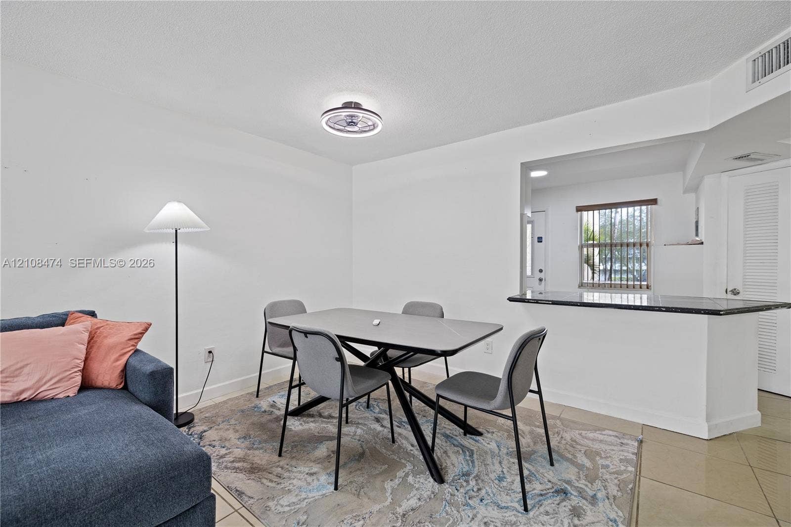 1501 NE 191st Street, #C216, Miami, FL 33179 Open-concept interior featuring stone-surfaced pass-through counter, neutral tile flooring, and integrated ceiling-mounted light fixture