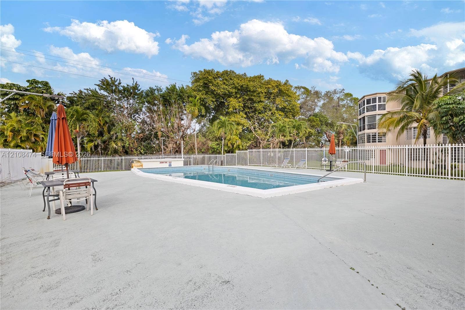 1501 NE 191st Street, #C216, Miami, FL 33179 In-ground swimming pool featuring a concrete deck, perimeter fencing, and mature landscaping