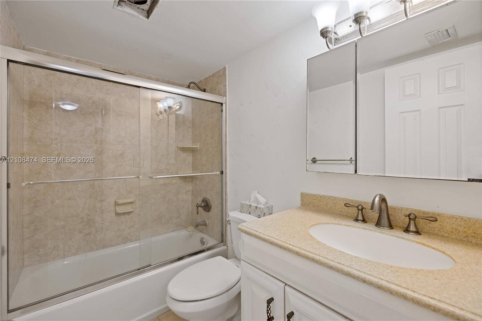 1501 NE 191st Street, #C216, Miami, FL 33179 Bathroom featuring a vanity with a solid-surface countertop, an undermount oval sink, metallic finish widespread faucet, mirrored medicine cabinet, and a shower-tub combination with sliding glass doors and tiled surround