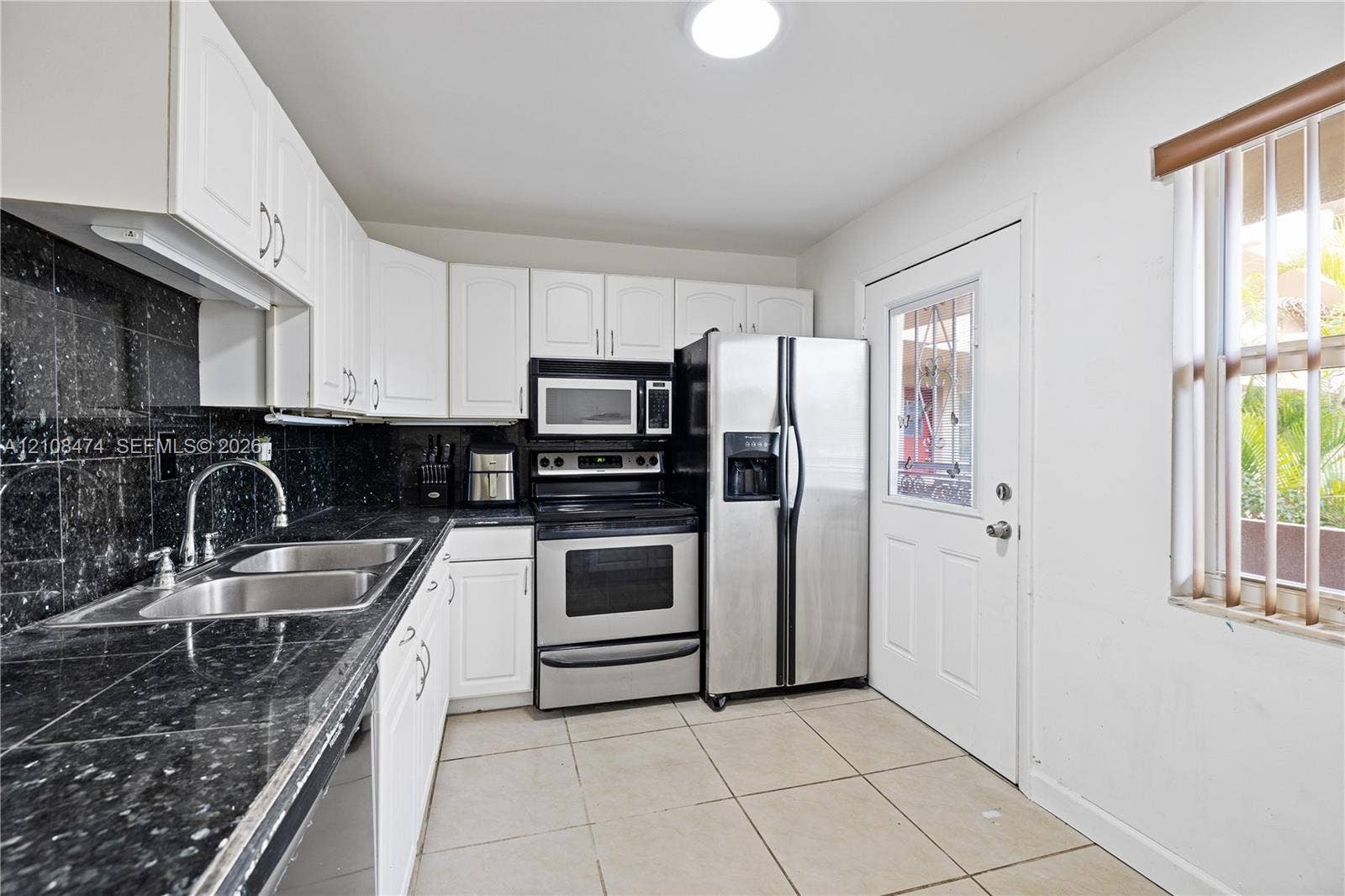 1501 NE 191st Street, #C216, Miami, FL 33179 Kitchen featuring white shaker-style cabinetry, dark stone-finish countertops, tiled backsplash, stainless steel appliances, and large-format floor tile