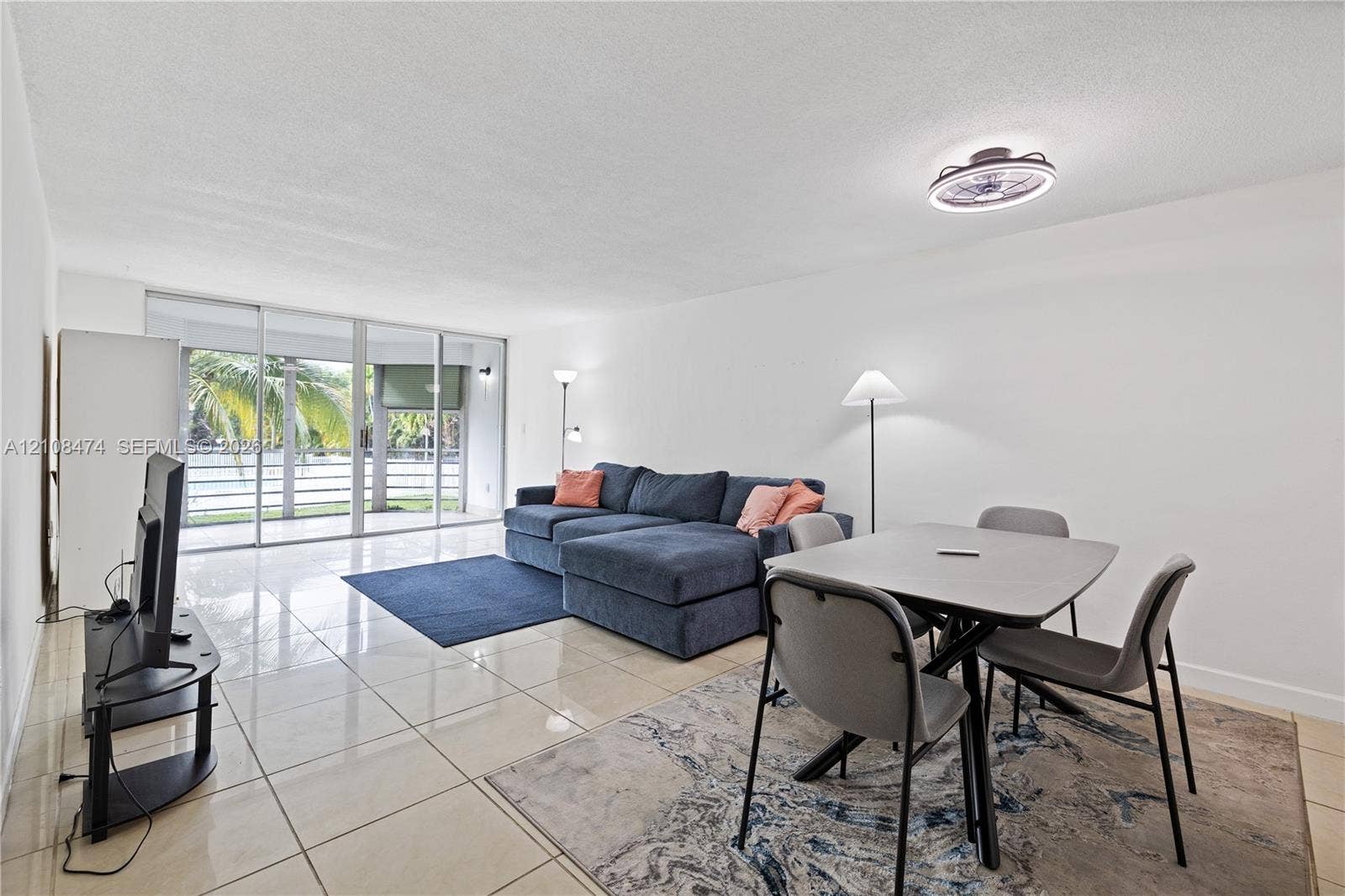 1501 NE 191st Street, #C216, Miami, FL 33179 Open-concept living space featuring high-gloss tile flooring, floor-to-ceiling sliding glass doors, and a flush-mount ceiling light fixture with an integrated fan