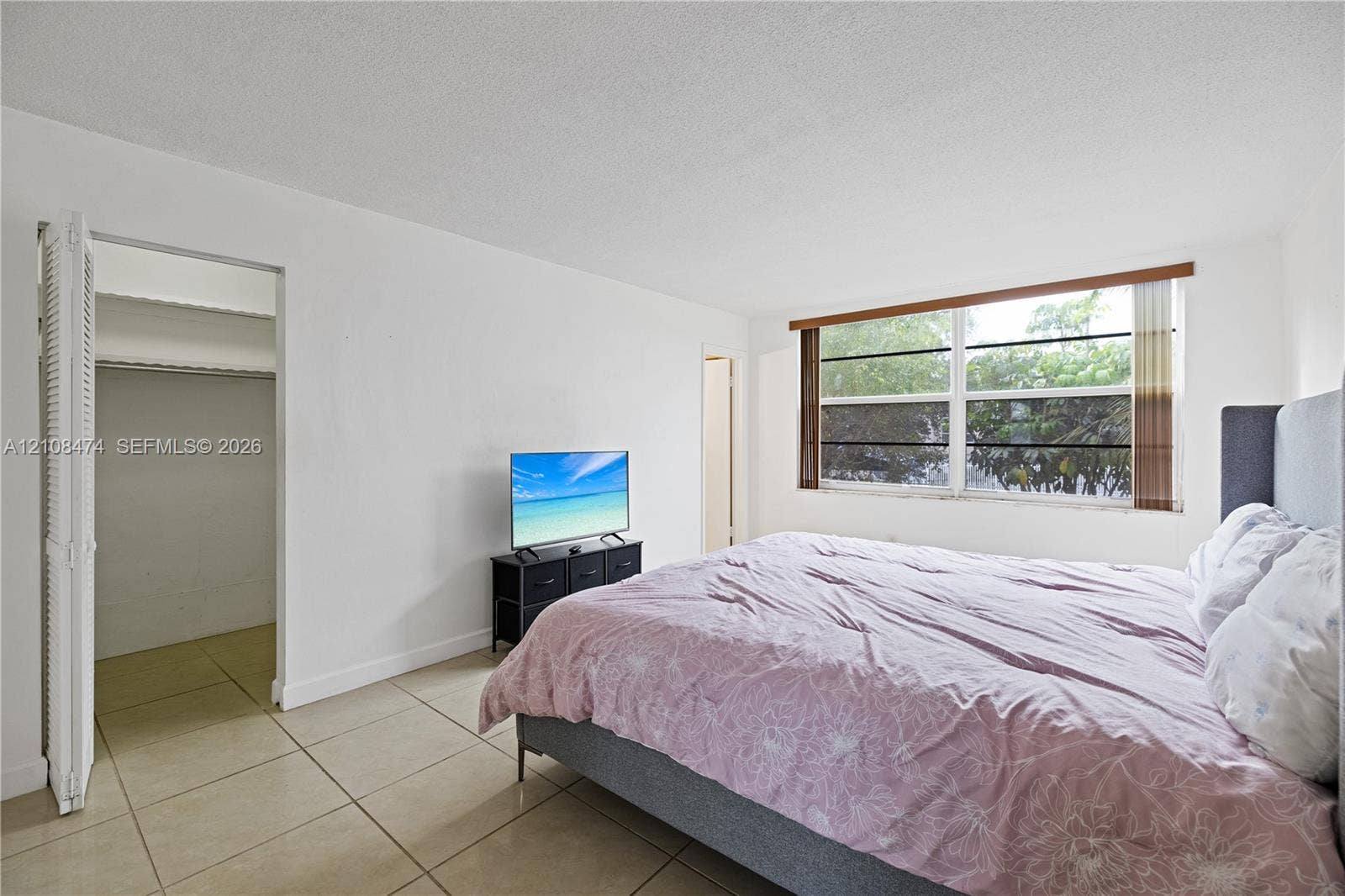 1501 NE 191st Street, #C216, Miami, FL 33179 Neutral-toned tile flooring, large multi-pane window with wood-finish trim, and walk-in closet with bi-fold door