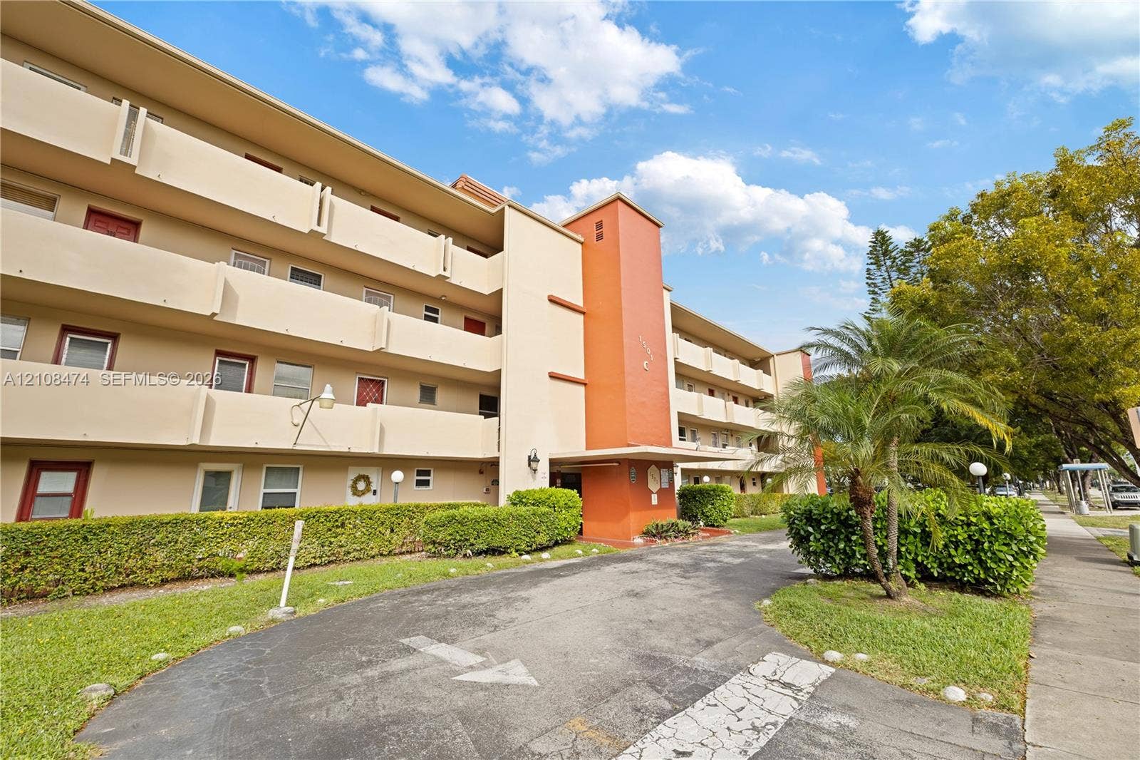 1501 NE 191st Street, #C216, Miami, FL 33179 Multi-story exterior featuring a stucco facade, accent orange pillar, private recessed balconies, and manicured landscaping