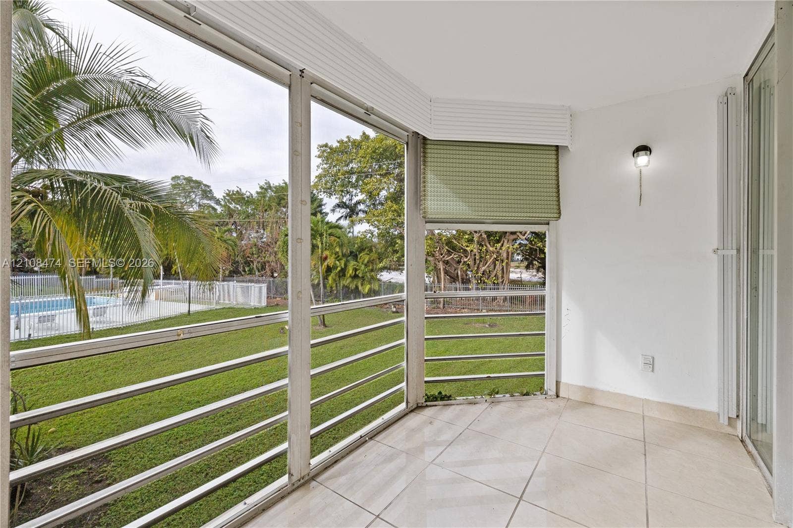 1501 NE 191st Street, #C216, Miami, FL 33179 Enclosed patio featuring light-toned tile flooring, floor-to-ceiling screen panels with horizontal railings, and a mounted wall sconce