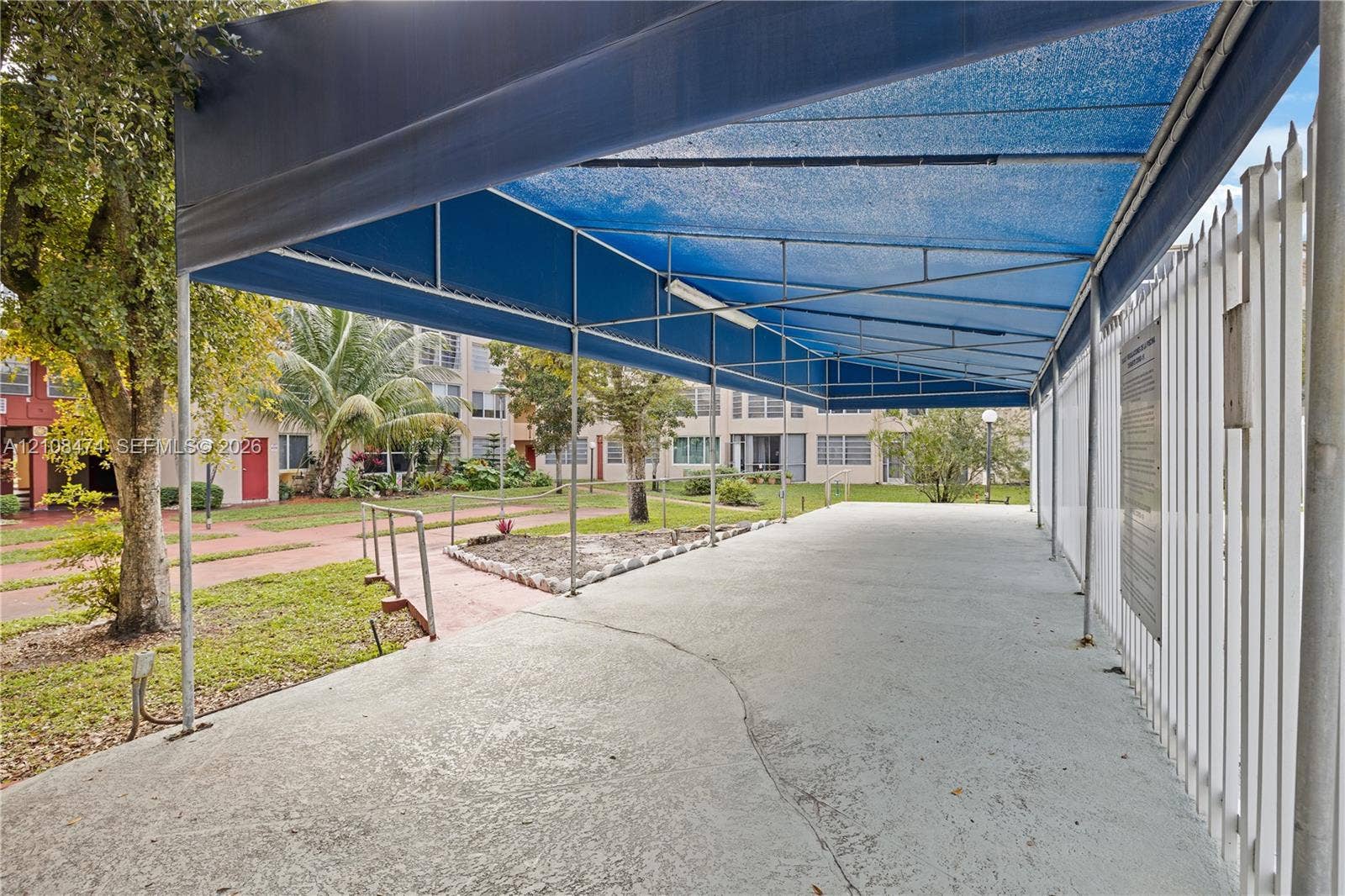 1501 NE 191st Street, #C216, Miami, FL 33179 Covered outdoor patio featuring a metal frame structure, blue shade canopy, concrete flooring, and perimeter metal fencing
