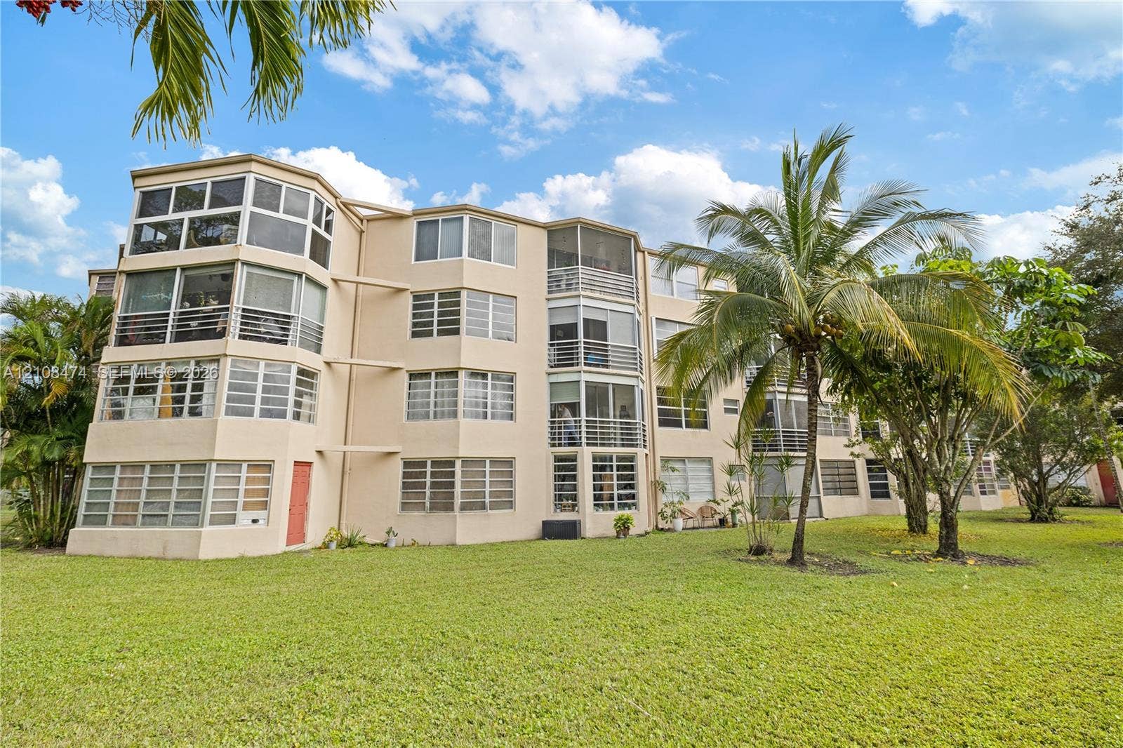 1501 NE 191st Street, #C216, Miami, FL 33179 Mid-rise exterior featuring multi-level screened-in lanais, light-toned stucco facade, and expansive lawn landscaping with mature palm trees
