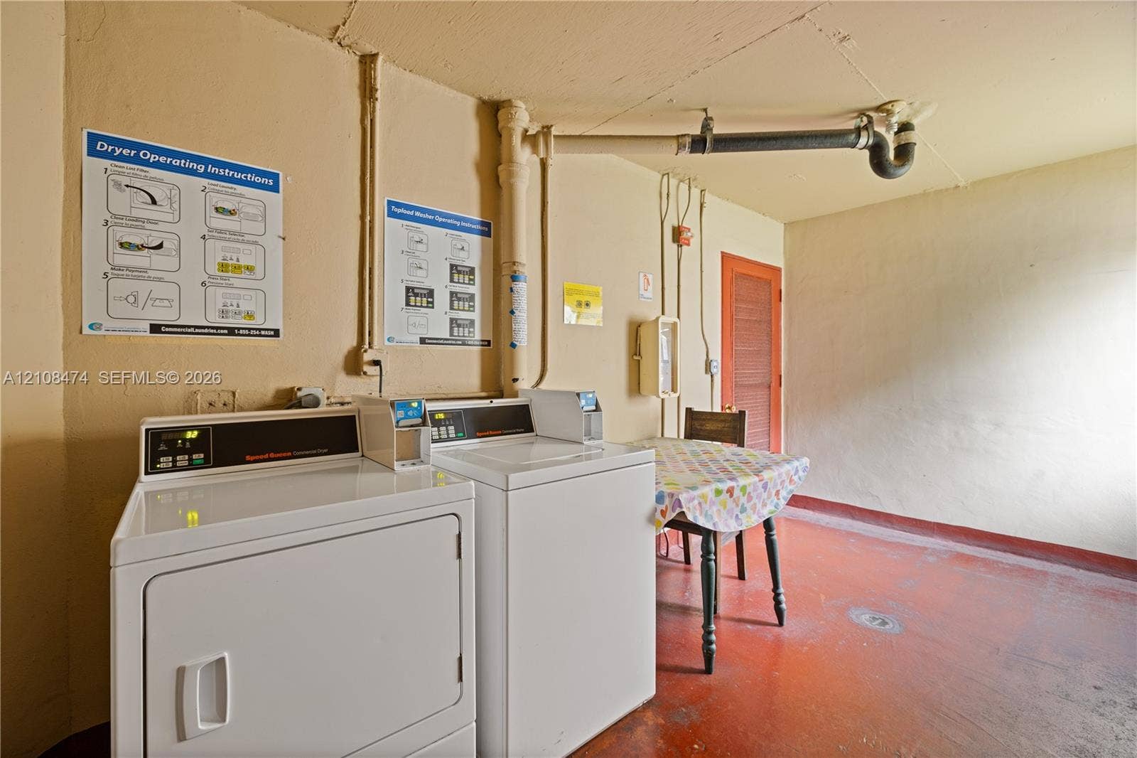1501 NE 191st Street, #C216, Miami, FL 33179 Utility area featuring two industrial-style, top-load laundry appliances, painted concrete flooring, and exposed overhead plumbing fixtures