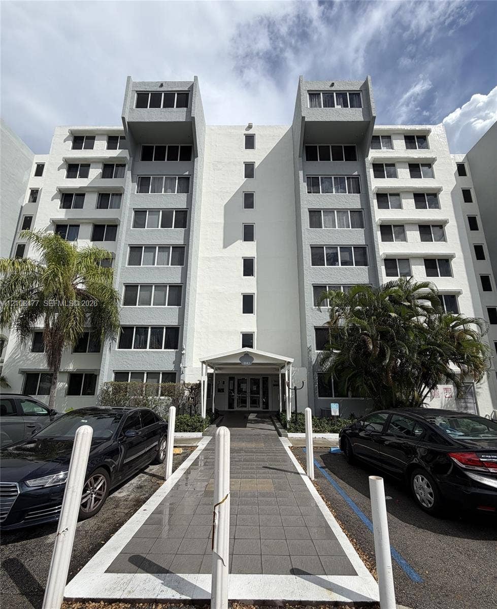 9143 SW 77th Avenue, #B708, Miami, Miami, FL 33156 Mid-rise residential building featuring a textured stucco facade, cantilevered upper-level projections, and a covered entryway with a stone-paved walkway