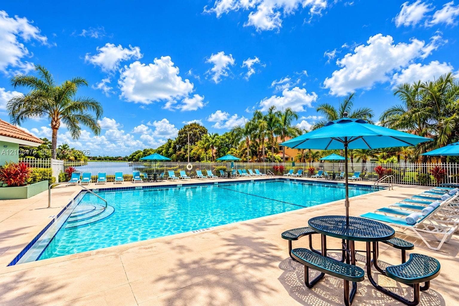 2233 NW 162nd Terrace, Pembroke Pines, FL 33028 Rectangular swimming pool featuring a concrete deck, metal perimeter fencing, integrated entry steps, and a waterfront setting with mature palm trees