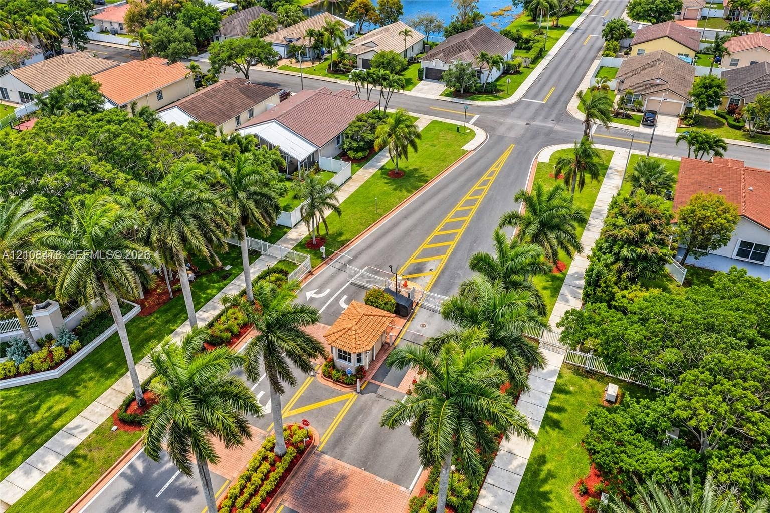 2233 NW 162nd Terrace, Pembroke Pines, FL 33028 Gated residential entrance featuring a tiled guard house, paved roadways, palm-lined landscaping, and extensive hardscaping