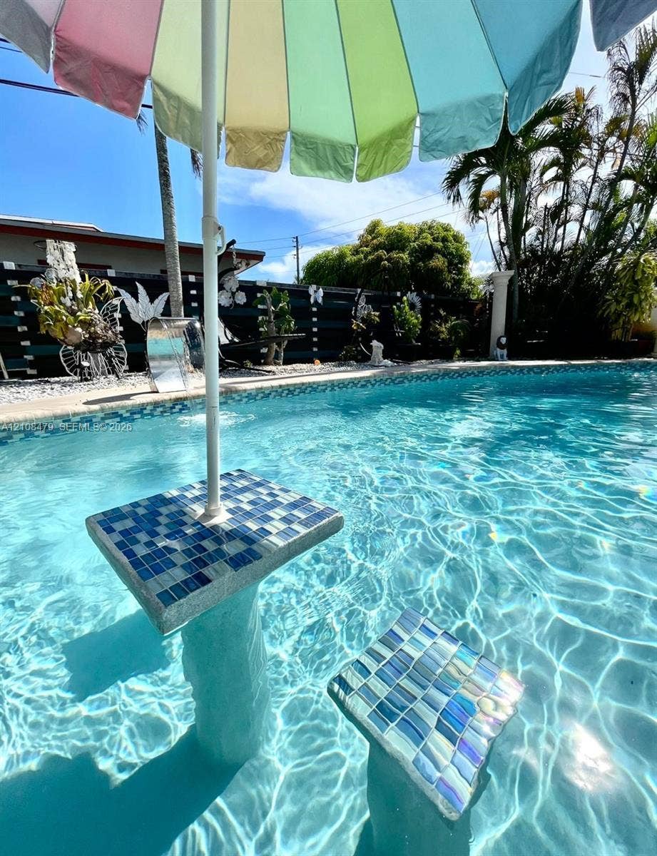 In-ground swimming pool featuring a tiled, built-in pedestal table and submerged seating with iridescent mosaic finish