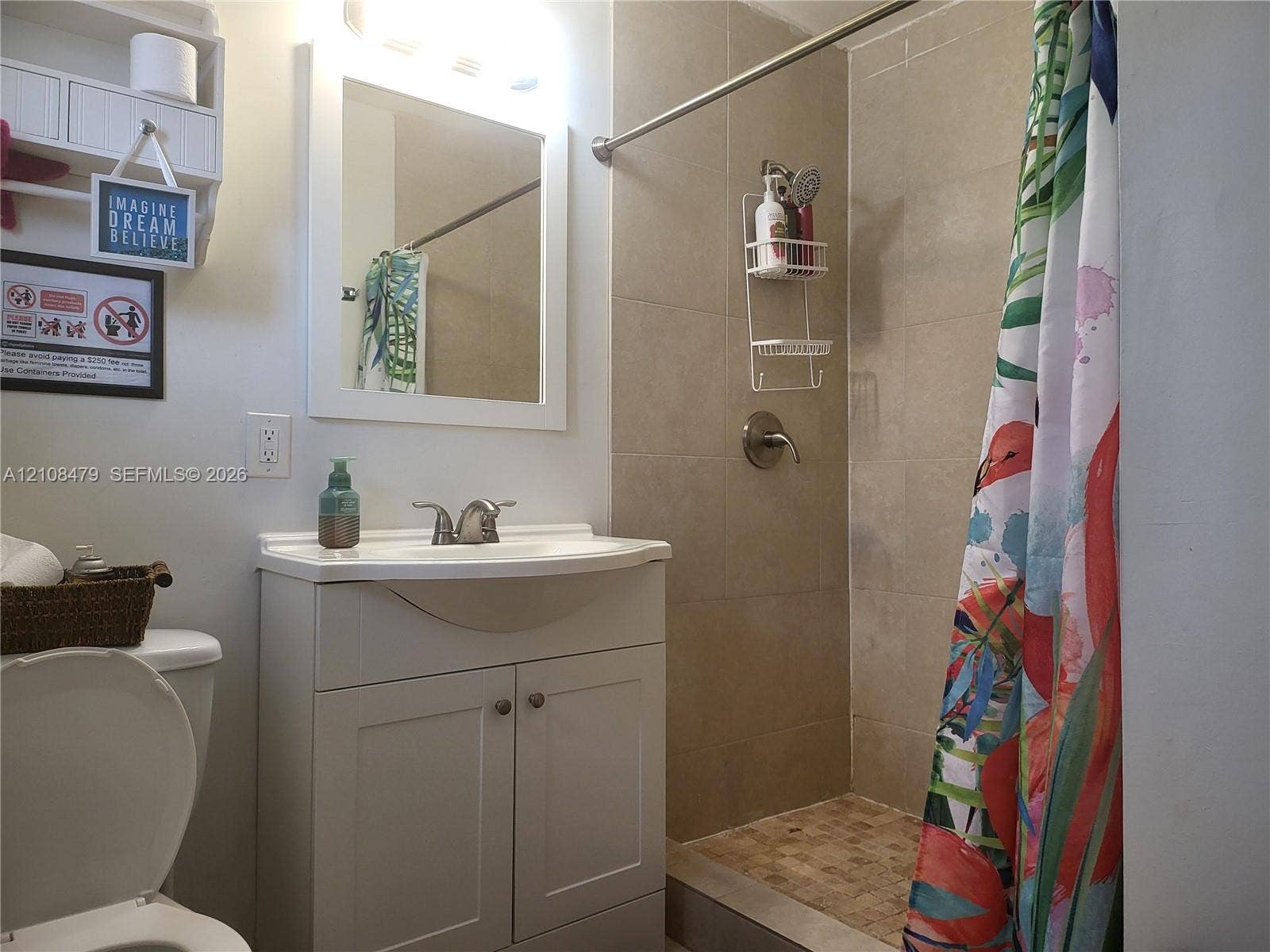 Bathroom featuring a white vanity cabinet with an integrated basin, wall-mounted mirror, built-in shelving unit, and a tiled shower enclosure