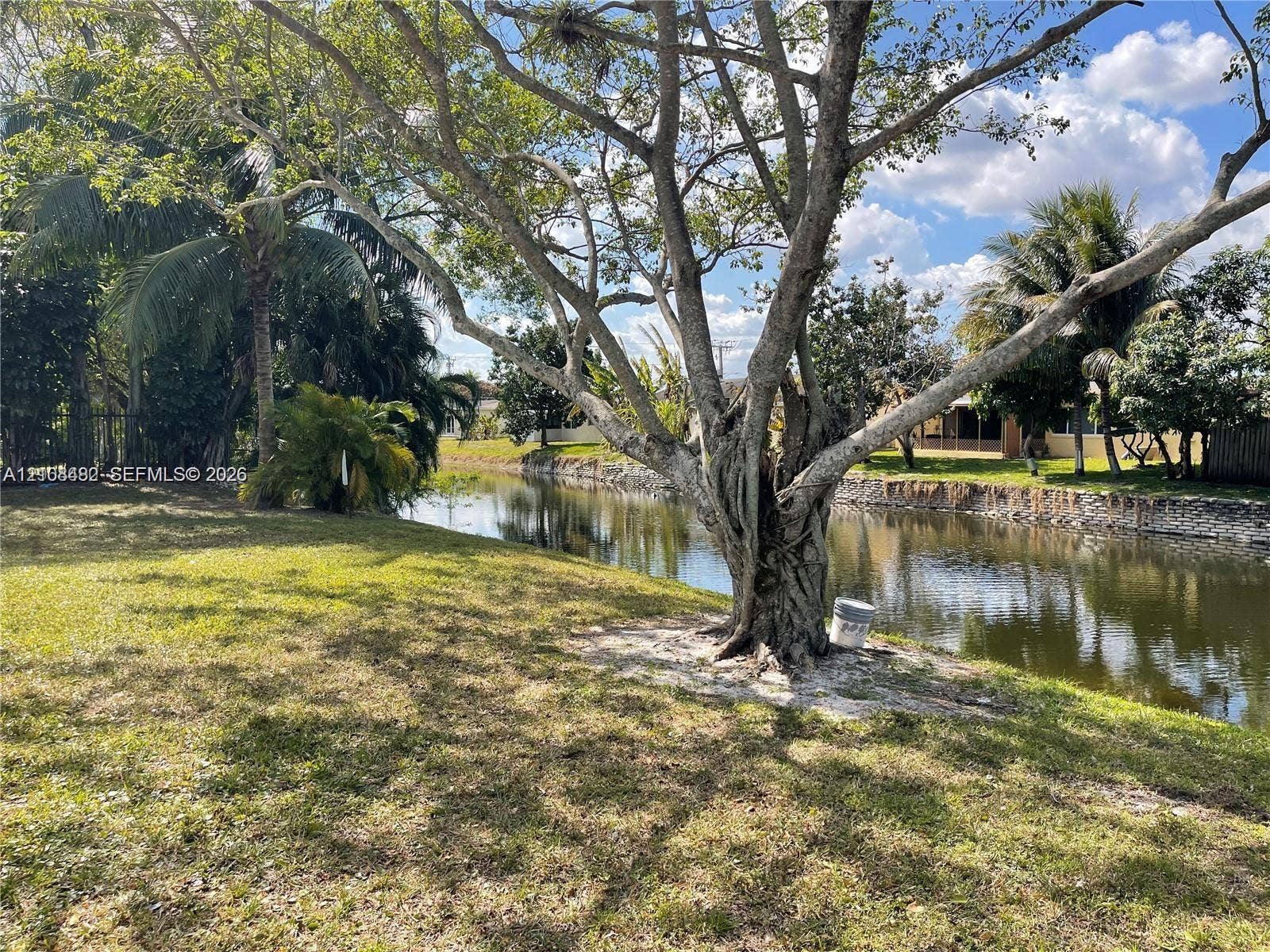 Waterfront backyard featuring mature trees, a manicured lawn, and a stone-lined canal bulkhead