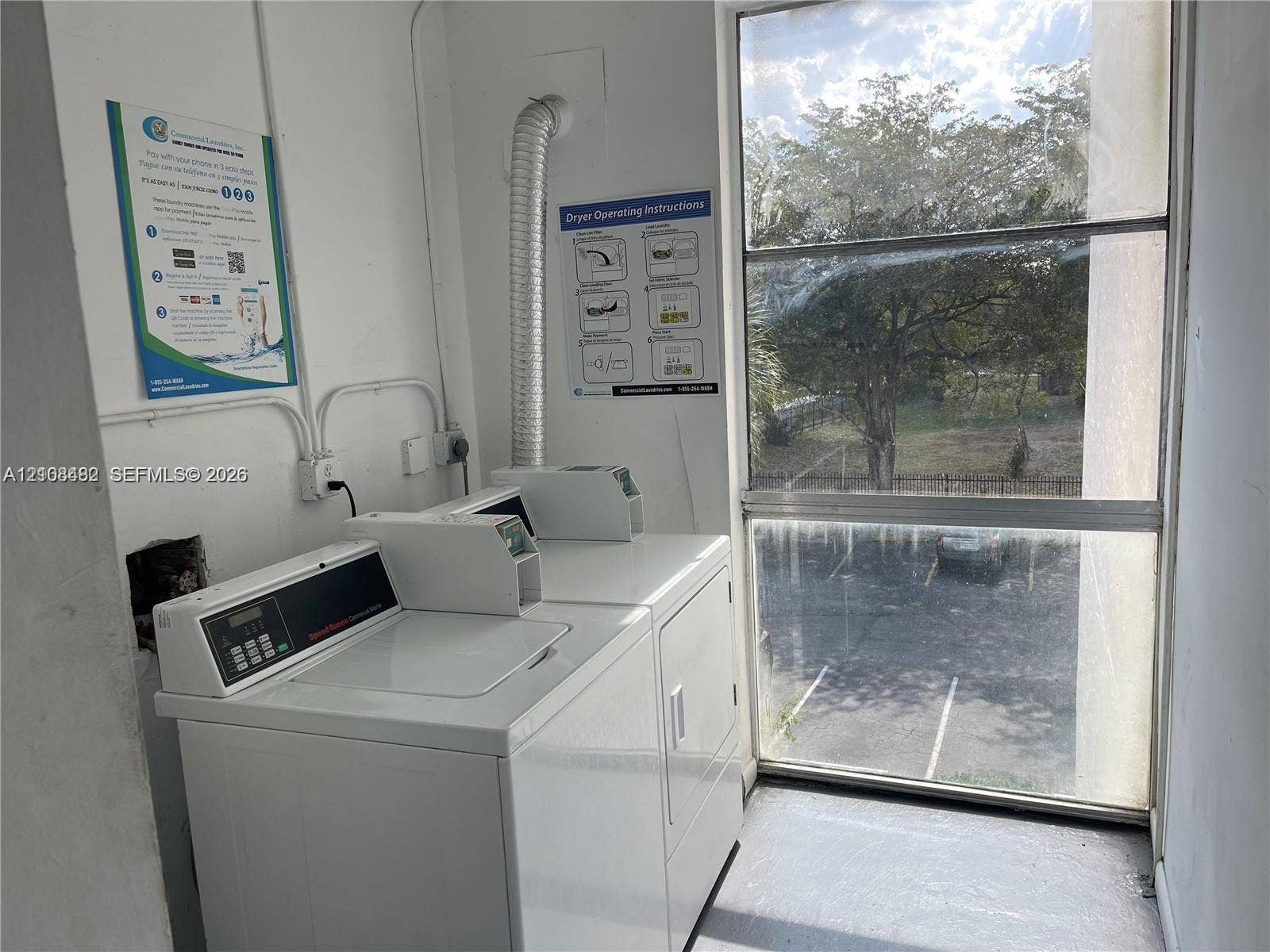 Laundry area featuring coin-operated washer and dryer units, a multi-pane fixed window, and a metal dryer vent