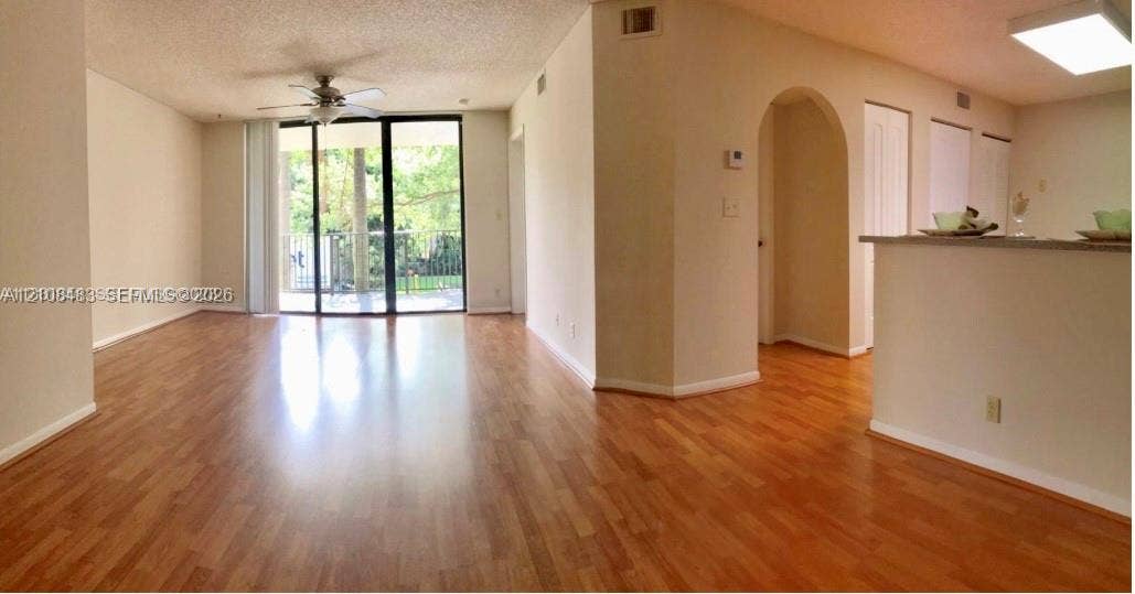 10121 W Sunrise Boulevard, #204, Plantation, Plantation, FL 33322 Open-concept living space featuring wood-finish flooring, sliding glass doors, a ceiling fan, and a prominent arched entryway