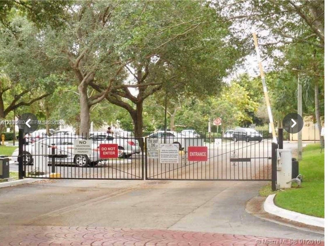 10121 W Sunrise Boulevard, #204, Plantation, Plantation, FL 33322 Gated entry featuring a metal vehicle barrier and mature perimeter trees