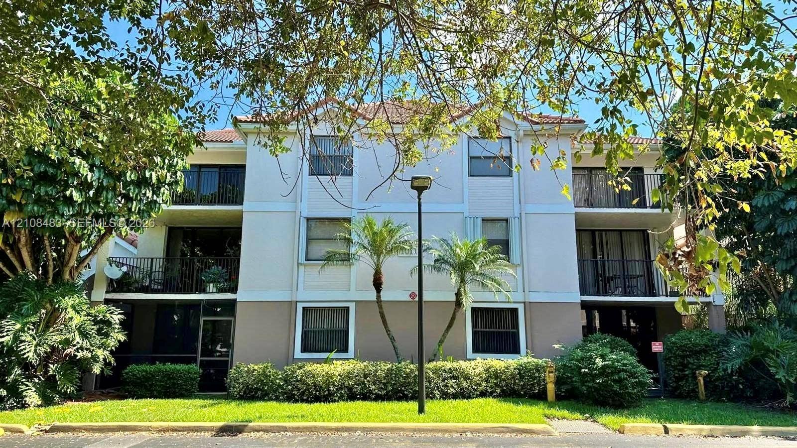 10121 W Sunrise Boulevard, #204, Plantation, Plantation, FL 33322 Three-story multi-unit structure featuring a stucco exterior, integrated private balconies, tile roofing, and mature landscaping
