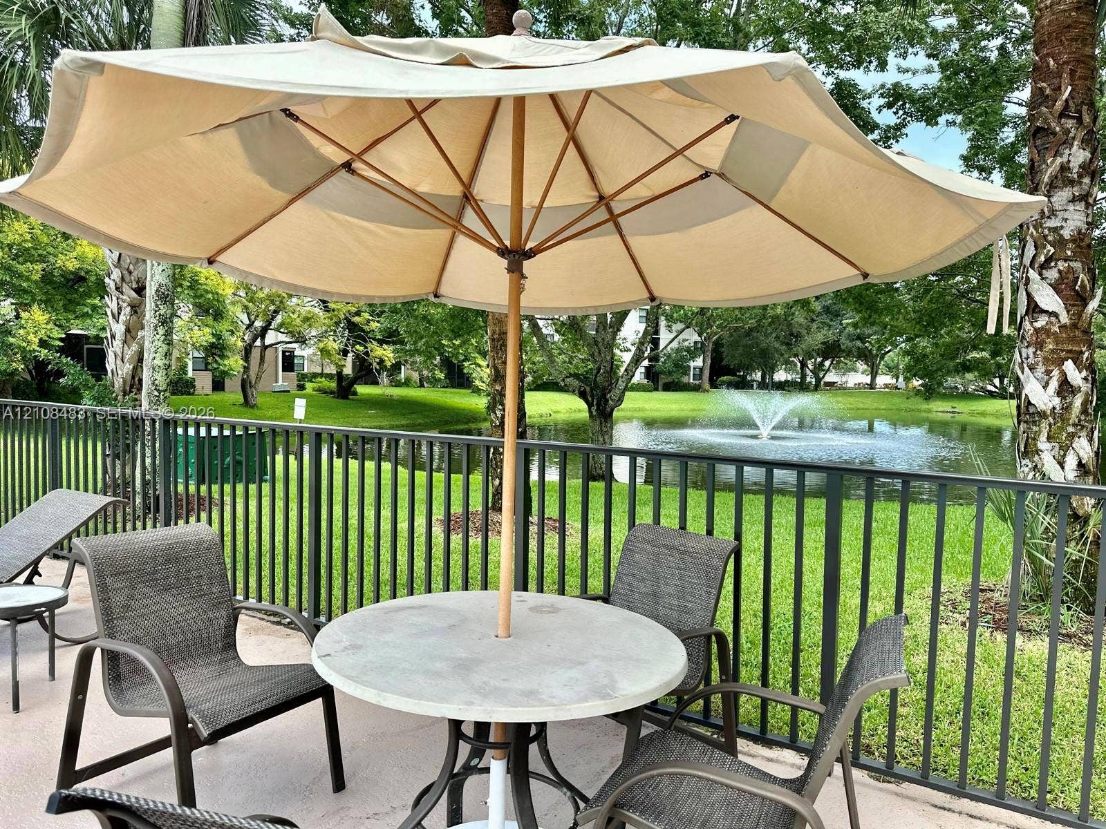 10121 W Sunrise Boulevard, #204, Plantation, Plantation, FL 33322 Outdoor patio area featuring a concrete deck, dark metal perimeter fencing, and water feature backdrop