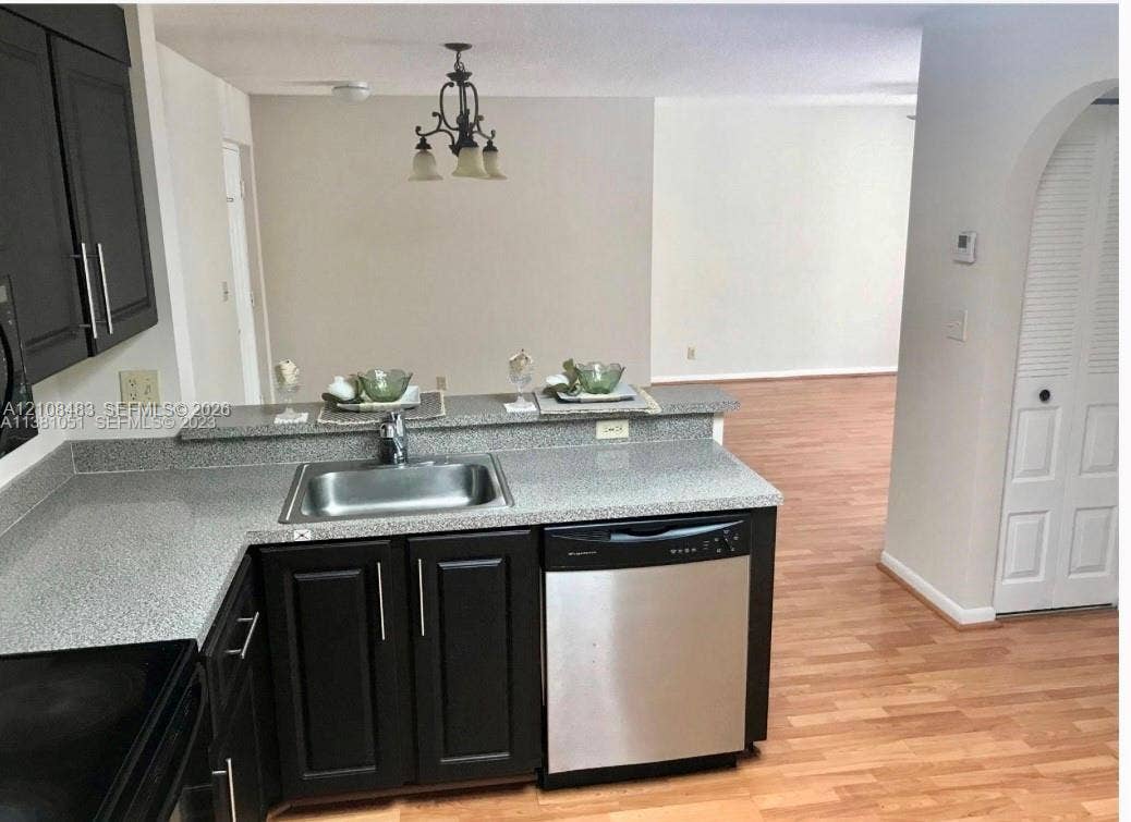 10121 W Sunrise Boulevard, #204, Plantation, Plantation, FL 33322 Kitchen featuring dark cabinetry, stone-finish countertops, stainless steel undermount sink, built-in dishwasher, and wood-finish flooring
