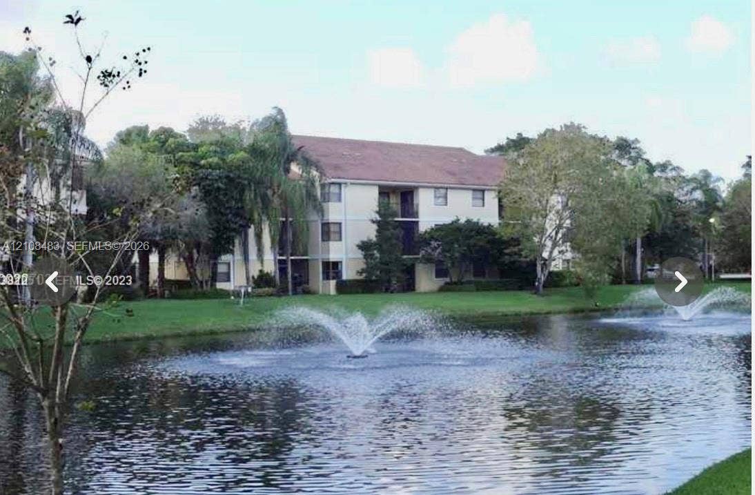10121 W Sunrise Boulevard, #204, Plantation, Plantation, FL 33322 Multi-story building exterior featuring a neutral facade, screened balconies, and a waterfront setting with decorative fountains and established landscaping