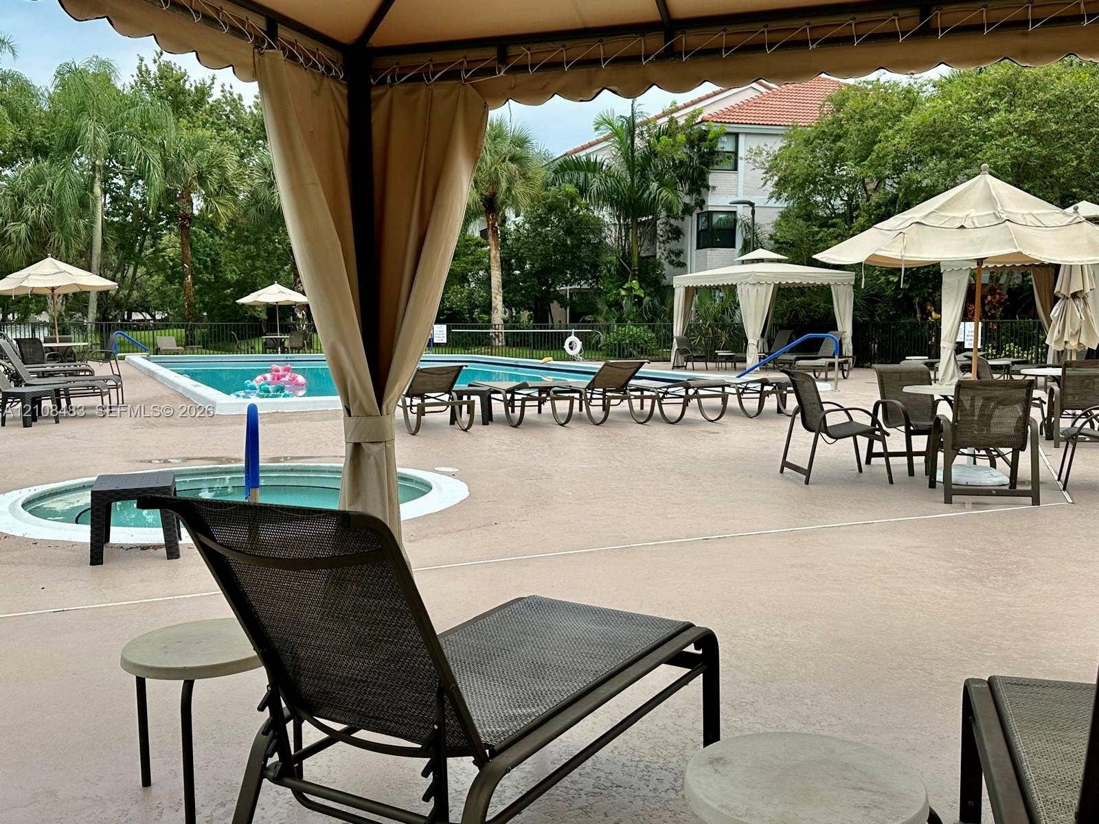10121 W Sunrise Boulevard, #204, Plantation, Plantation, FL 33322 Community swimming pool with an integrated spa, concrete deck, and multiple shaded gazebo structures