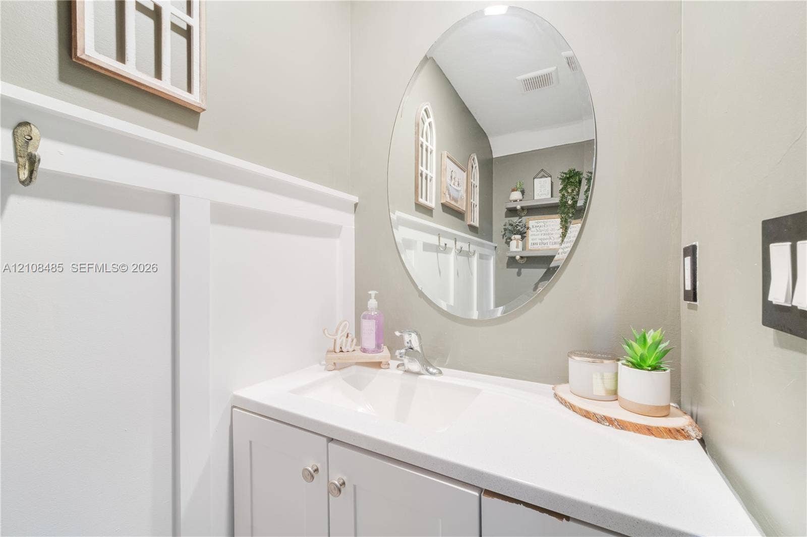 10217 SW 231st Lane, Miami, FL 33190 Oval wall-mounted mirror, white vanity cabinet with a integrated sink, polished chrome faucet, and board-and-batten wall detailing