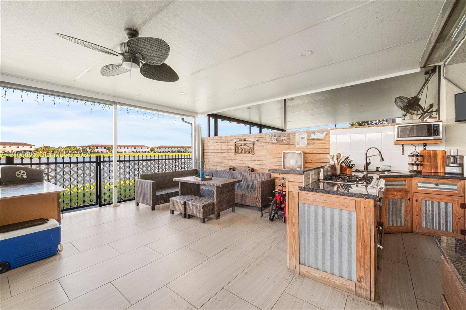 10217 SW 231st Lane, Miami, FL 33190 Covered patio featuring large-format tile flooring, a ceiling fan, and a built-in outdoor kitchen with stone-finish countertops, wood cabinetry with metal paneling, and a high-arch faucet